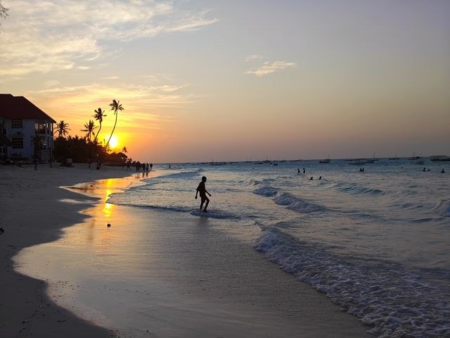 Sunset on a Zanzibar beach with palms and a walker on the sand