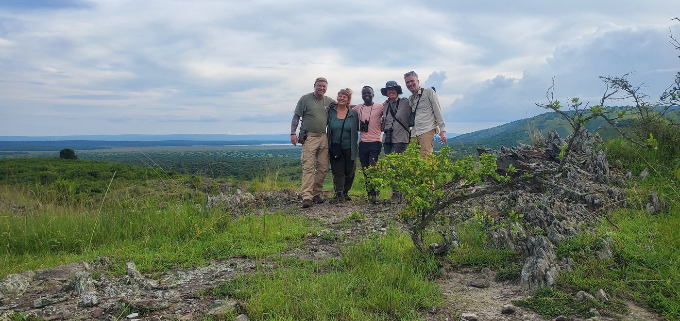 Guests and guide with binoculars on a ridge above green plains and a distant lake