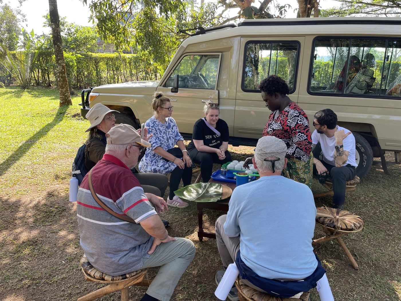 Guests gathered around a table in the shade beside the safari vehicle