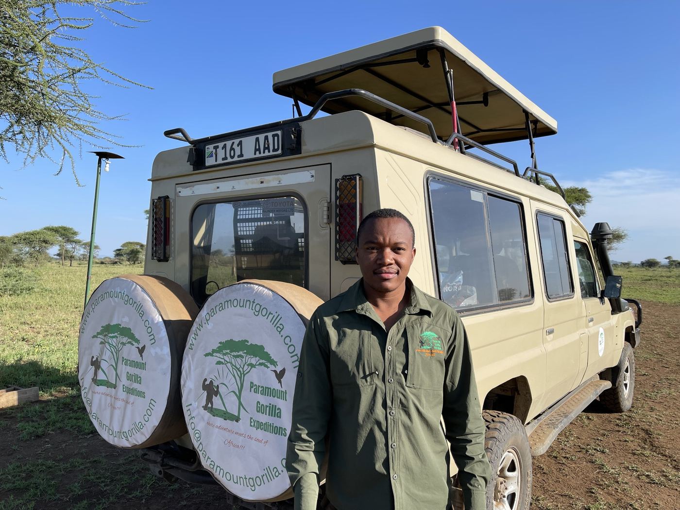 Safari guide standing in front of a Paramount Gorilla Expeditions safari vehicle with a pop-up roof