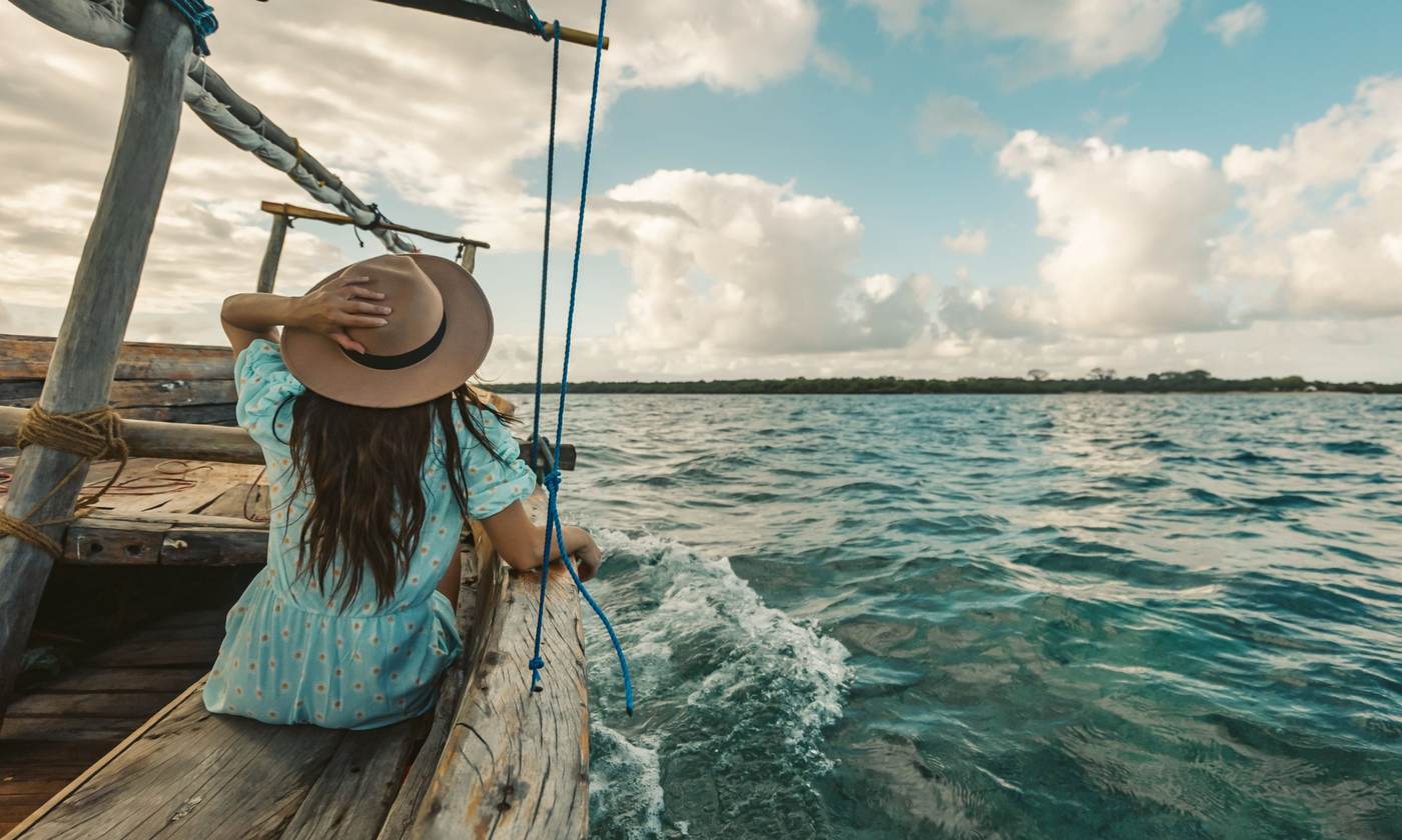 Traveller in a sun hat at the front of a wooden dhow