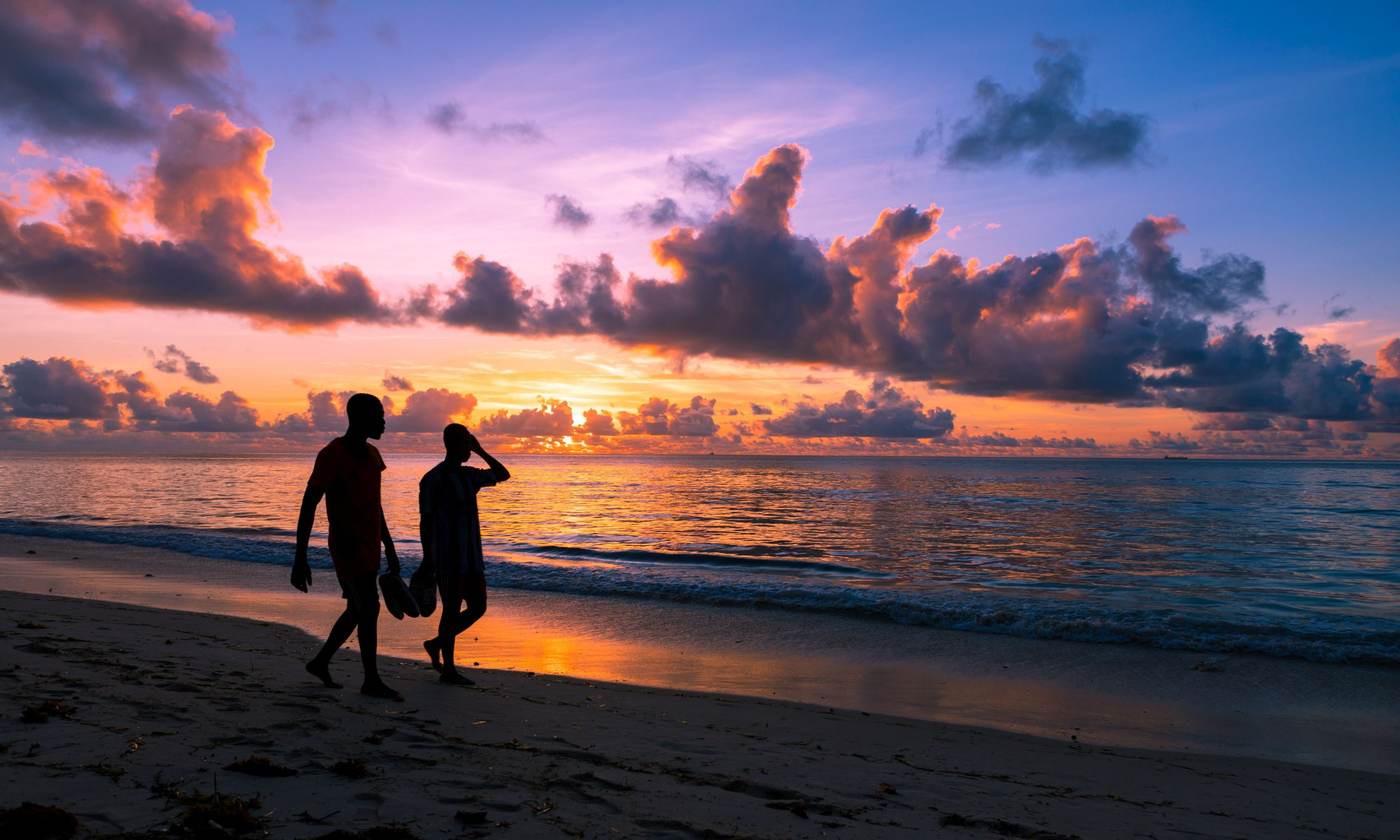 Two people walking along a beach at a colourful sunset