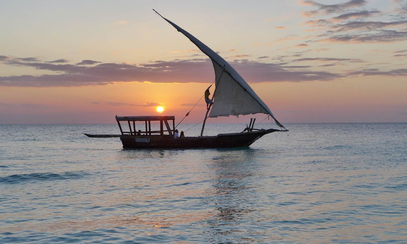 Wooden dhow with a white sail at sunset off Zanzibar